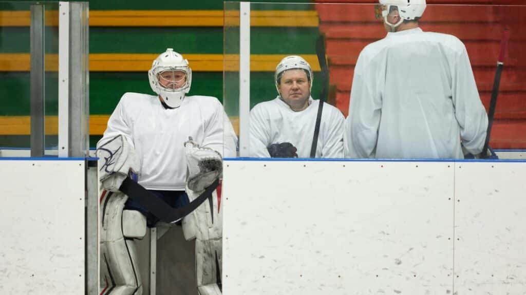 Hockey players in uniforms sitting on the bench during a game pause inside the ice rink.