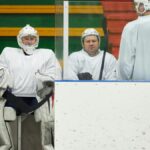 Hockey players in uniforms sitting on the bench during a game pause inside the ice rink.