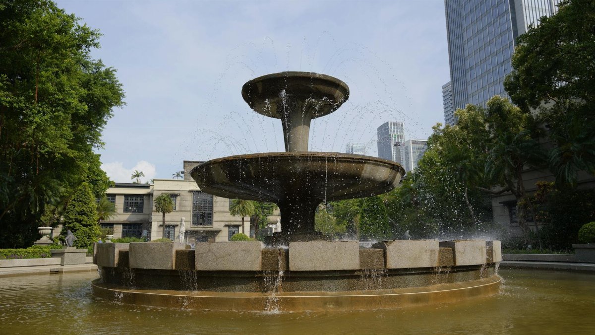 Elegant stone fountain in a tranquil Taipei park, surrounded by greenery and skyscrapers.
