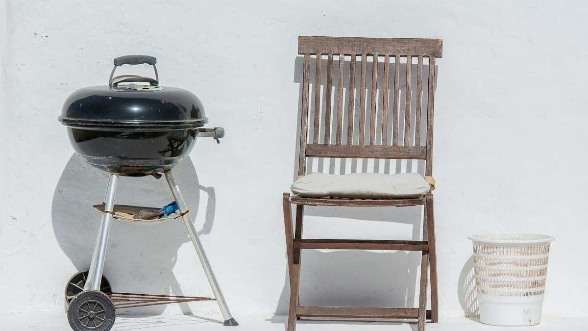 Outdoor scene with a barbeque grill, wooden chair, and white wall, evoking summer relaxation.