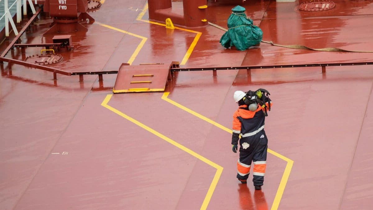 Workers on a cargo ship deck during daytime, wearing protective gear, ensuring safety compliance.