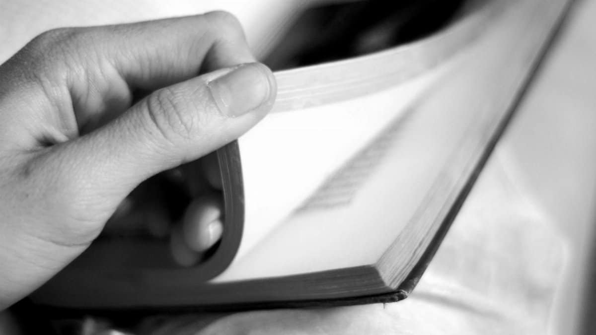 Artistic black and white close-up of a hand gently turning a book page, conveying contemplation and learning.