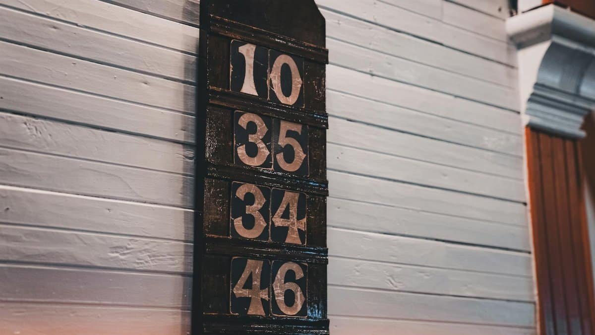 A close-up of a vintage wooden board displaying large numbers on a white wall.