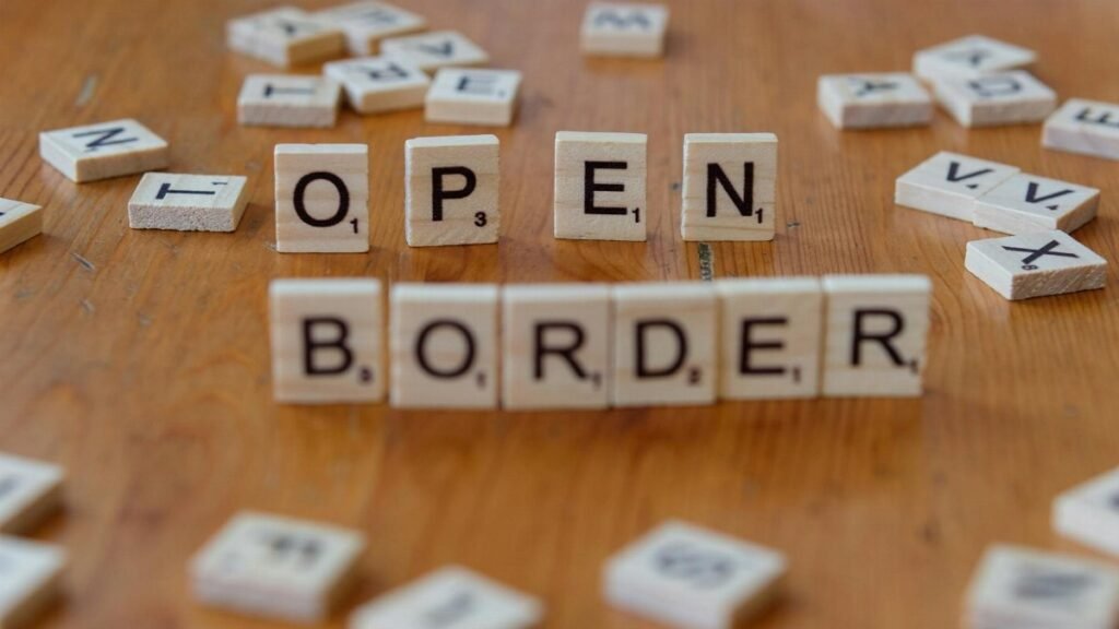 Wooden Scrabble letters on a table spelling out 'open border', concept of migration and geopolitics.