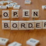 Wooden Scrabble letters on a table spelling out 'open border', concept of migration and geopolitics.