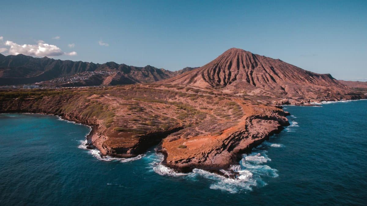 Breathtaking aerial view of a mountainous Hawaiian coastal landscape with clear blue ocean.