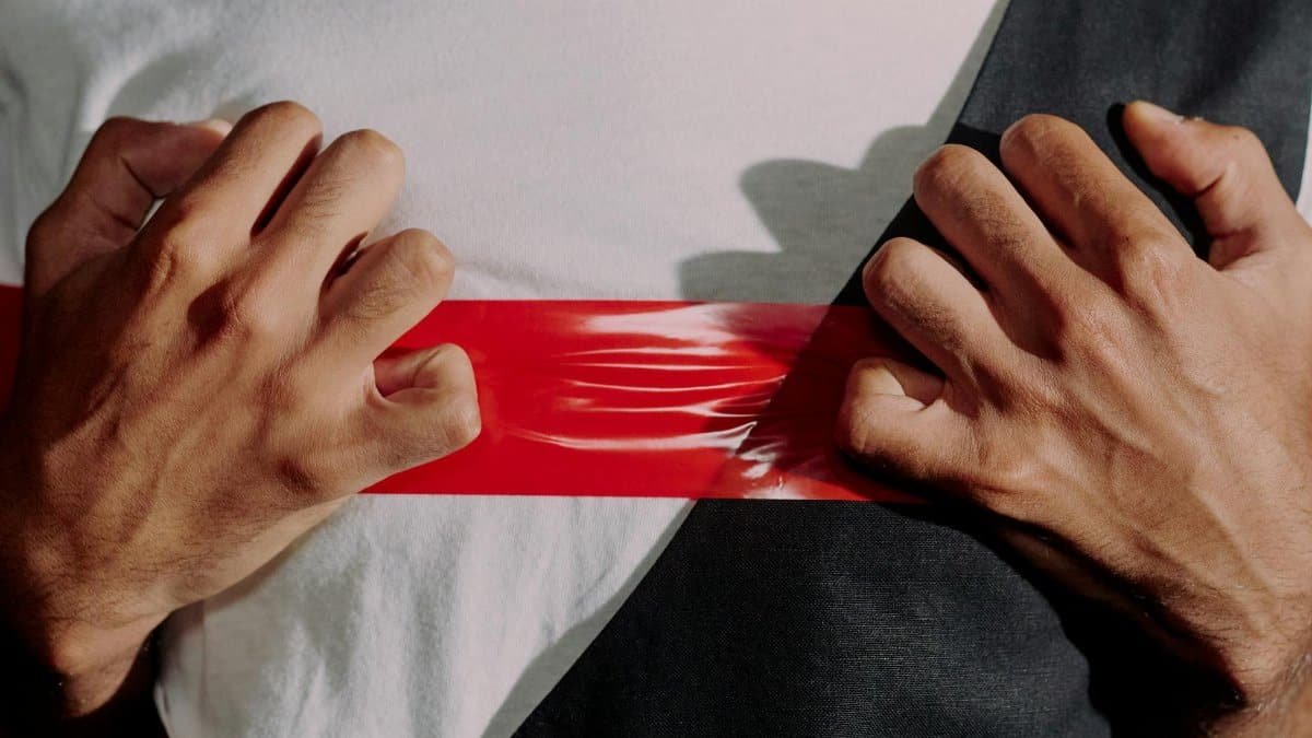 Close-up of hands holding and tearing red tape against a white and black background, symbolizing restriction.