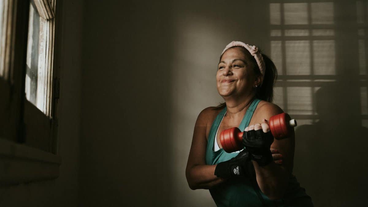 Confident middle-aged woman lifting dumbbells indoors, embracing a healthy lifestyle.