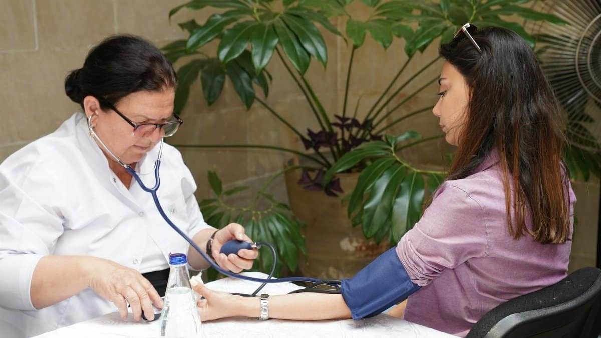 A healthcare worker measures a woman's blood pressure in an outdoor setting, emphasizing wellness and care.