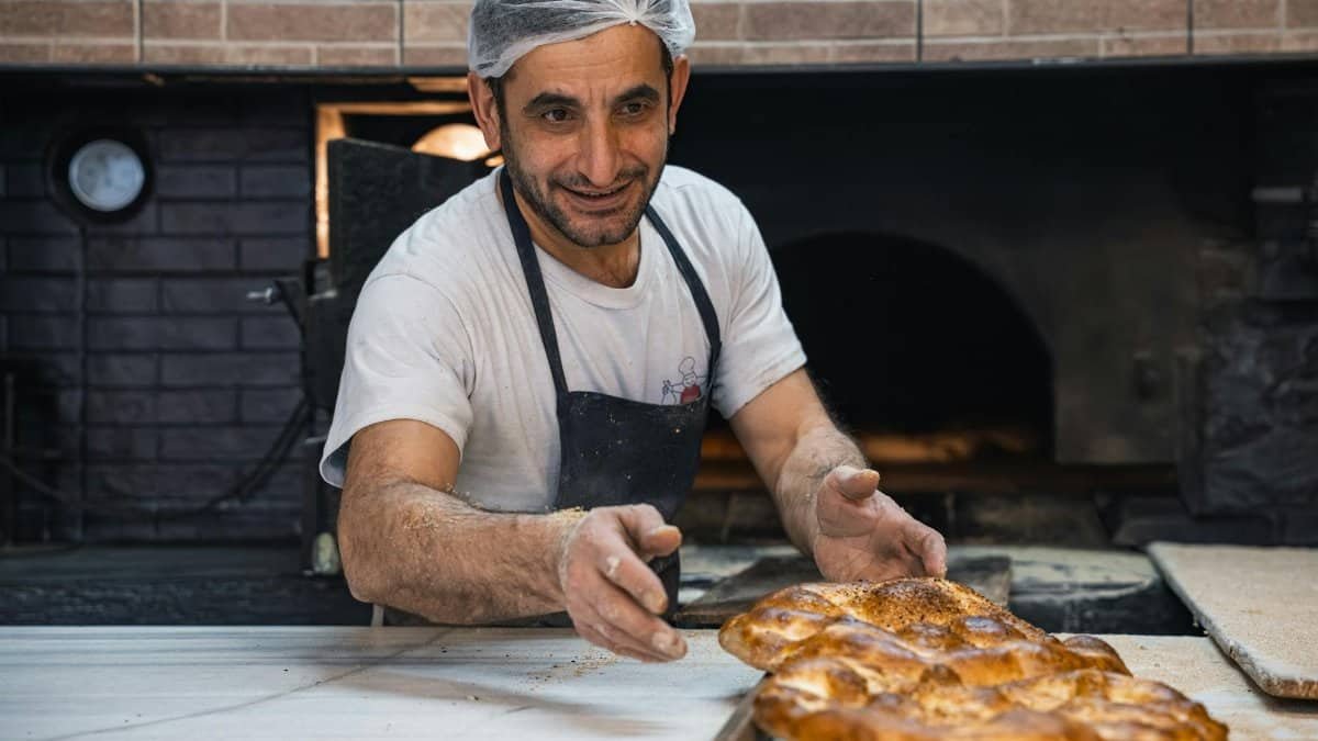 A skilled baker with a cheerful expression, preparing bread in a traditional bakery setting.