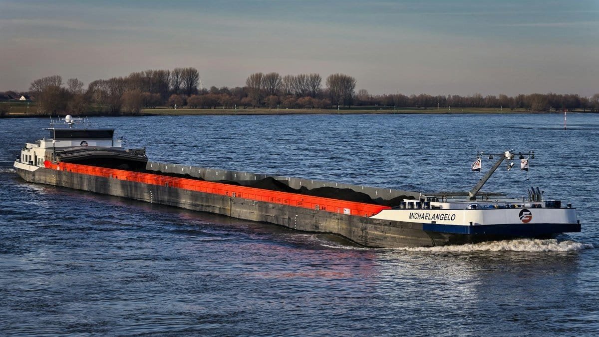 Large cargo ship navigating a calm inland waterway under clear skies.