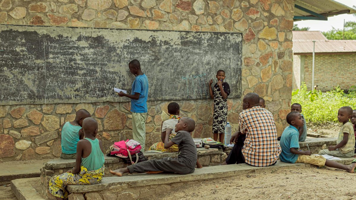 Children studying outdoors with a teacher, engaging with a blackboard at a rural school.