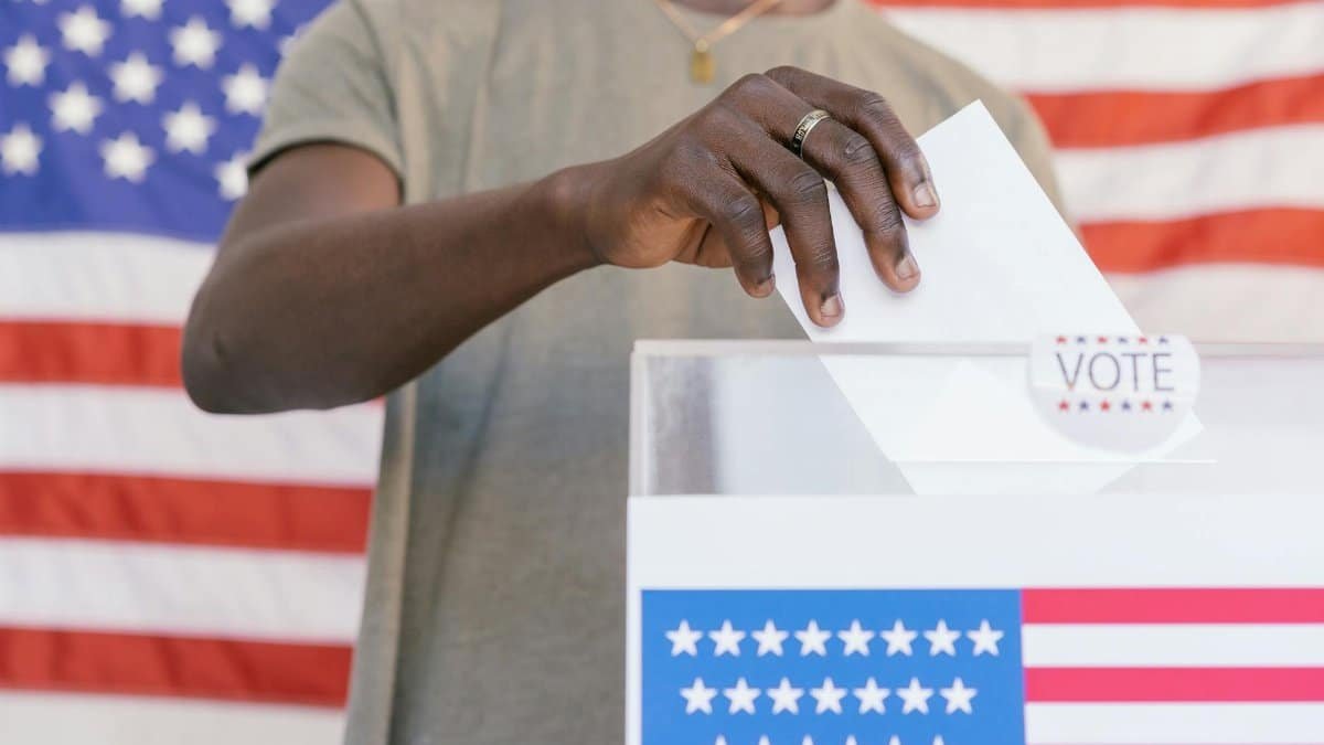A person casting their vote at a polling station with a US flag in the background.