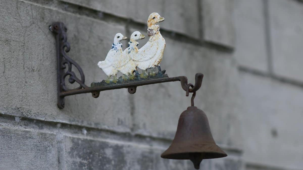 A vintage metal bell featuring an intricate duck figurine on a rustic wall. Perfect for decor enthusiasts.