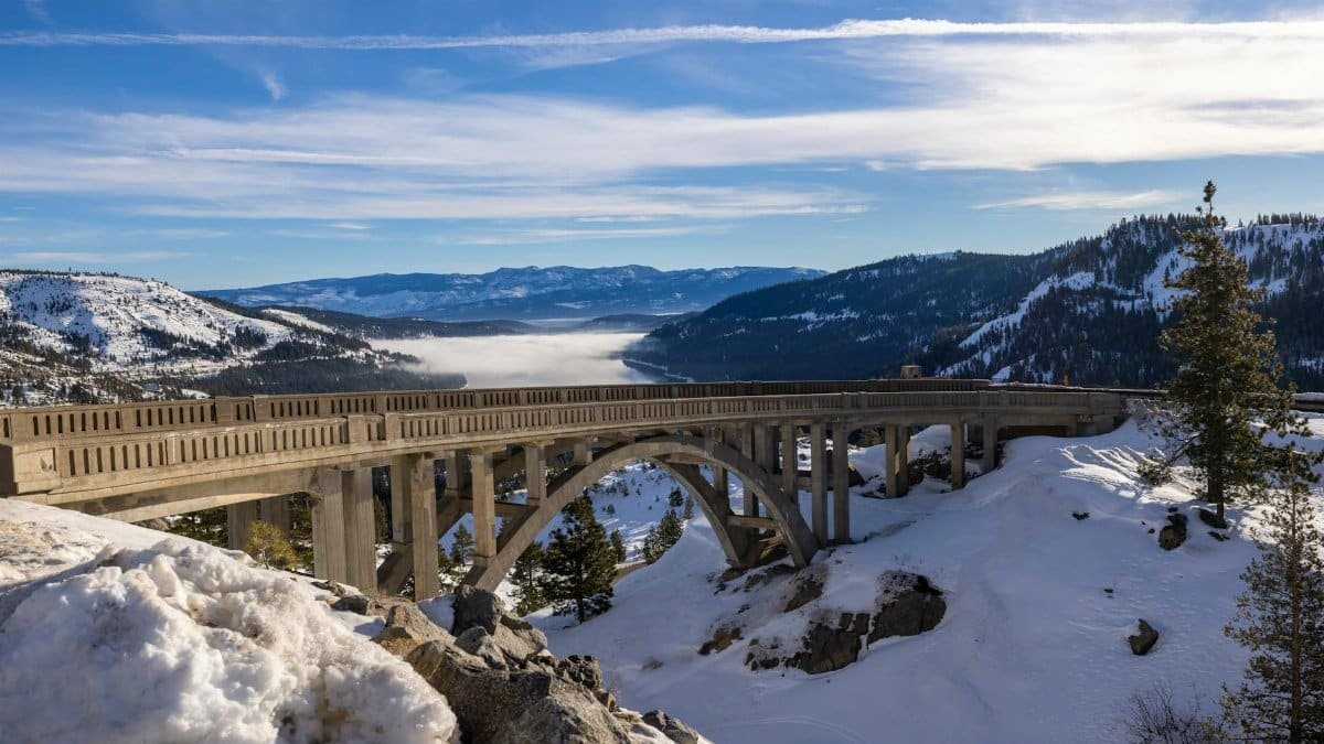 Breathtaking winter view of Donner Summit Bridge amidst snow-covered mountains and blue skies.