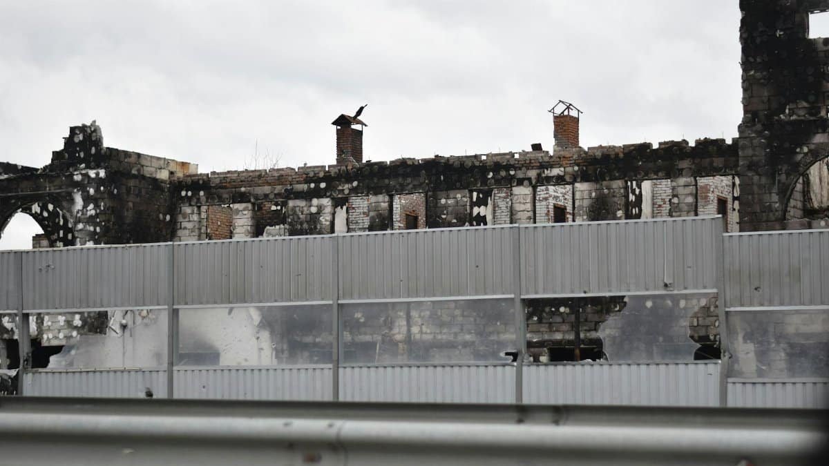 A destroyed building behind a metal noise barrier, hinting at past conflict.