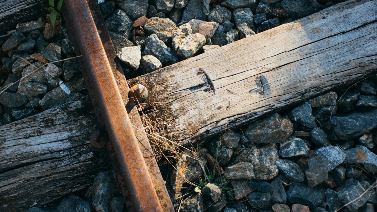 Close-up of a rusty railway track with wooden ties surrounded by rocks, exposed to sunlight.