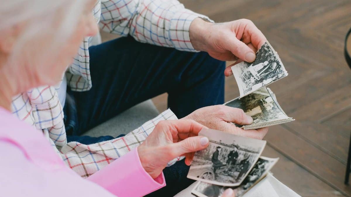 Elderly couple reminiscing over vintage black and white photographs, exploring memories.