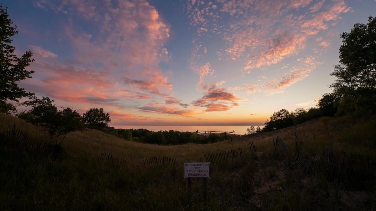 Dramatic sunset over Mount Pisgah dunes in Holland, Michigan with vibrant clouds and serene landscape.