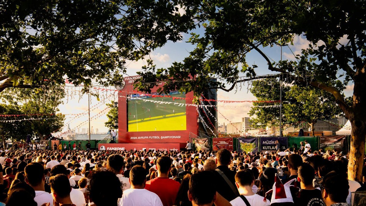 Crowd gathered in İstanbul park watching Euro football on big screen. Energetic summer atmosphere.