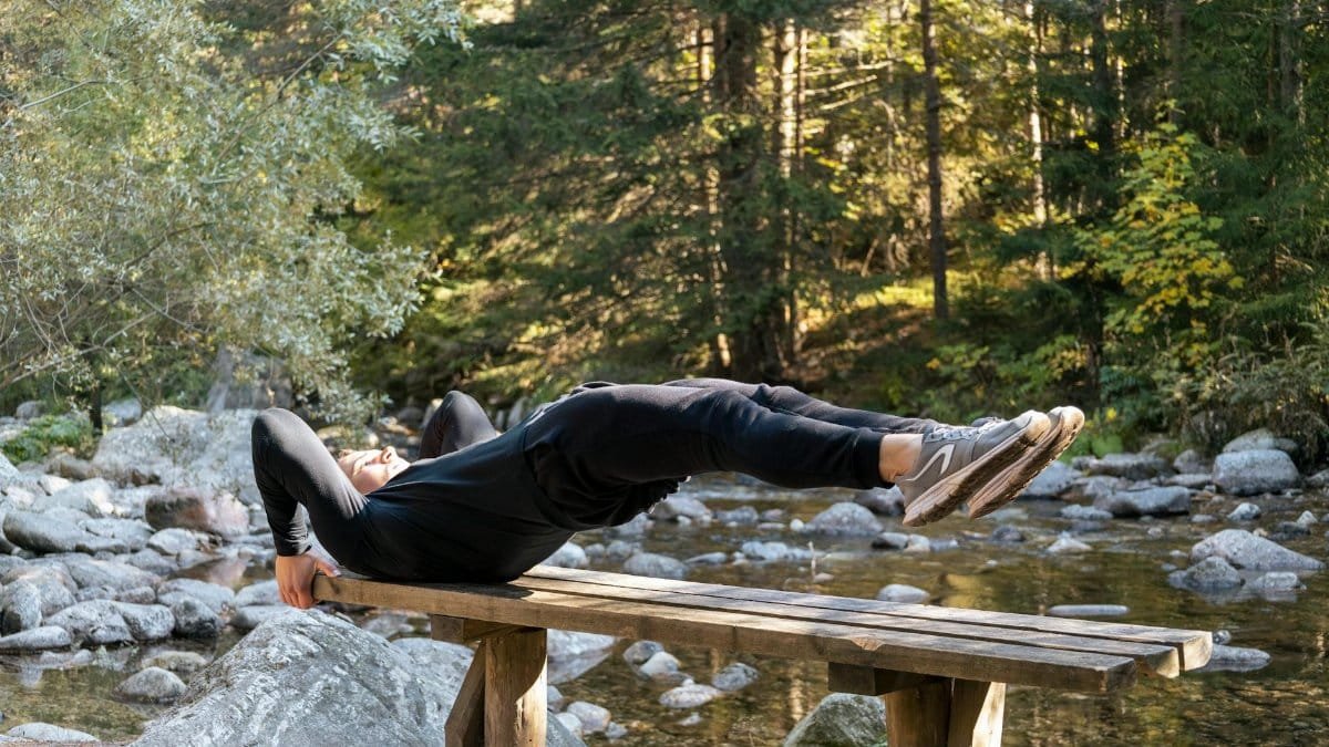 Man performing a core exercise on a bench by a serene river in a forest setting.