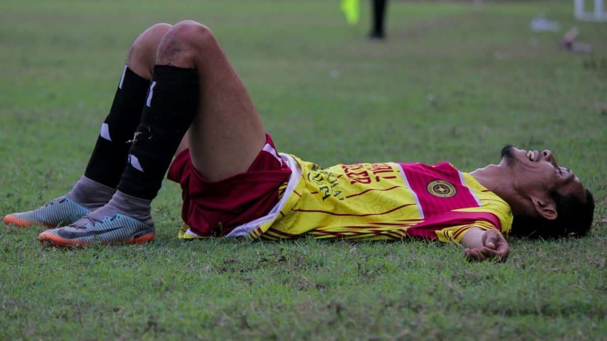 A tired soccer player lies on the grass field after an intense match.