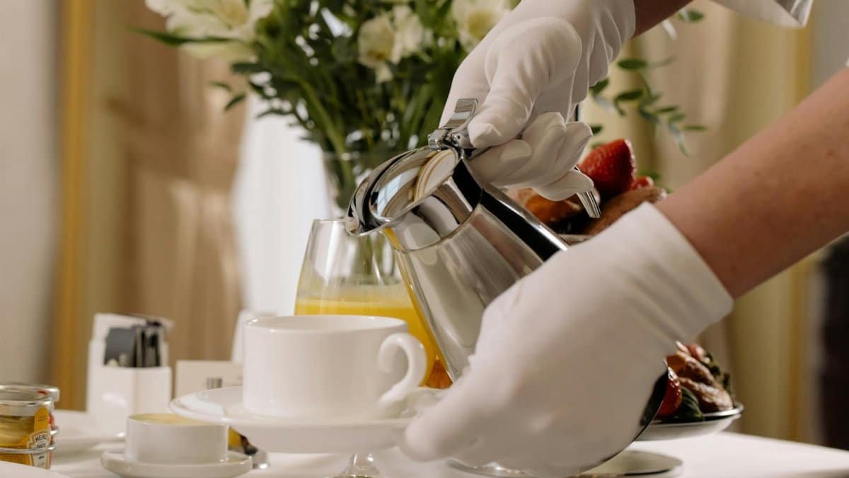Elegant room service setting with coffee being poured by gloved hands in a hotel.