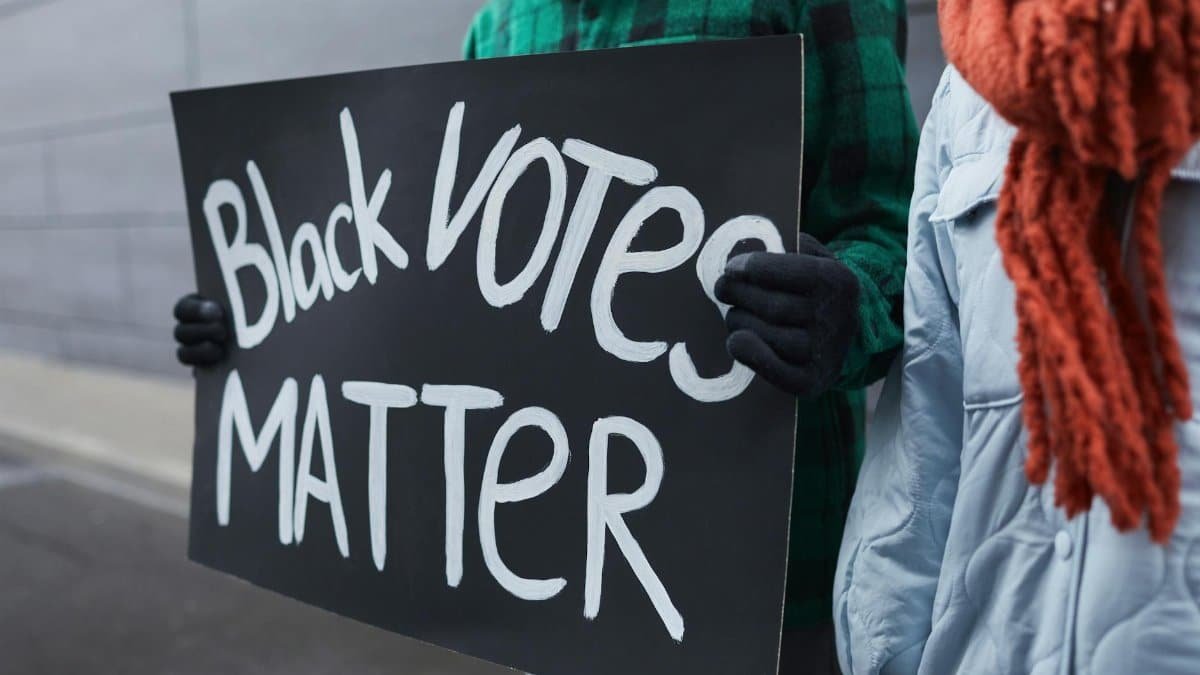 Two people holding a 'Black Votes Matter' sign in winter clothing, outdoors.