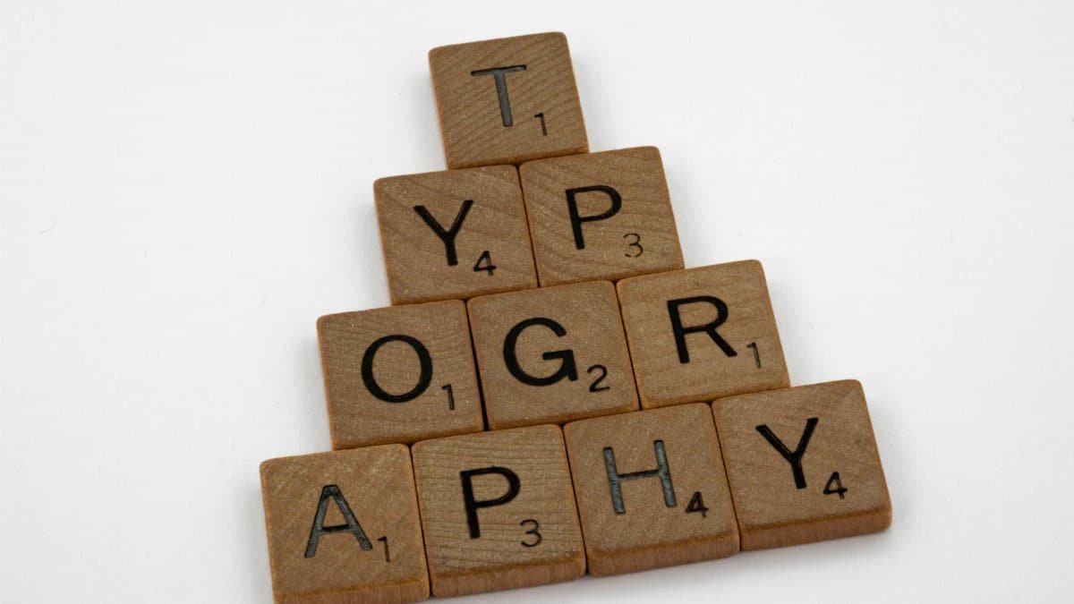 Close-up of wooden Scrabble tiles forming the word typography on a white background.