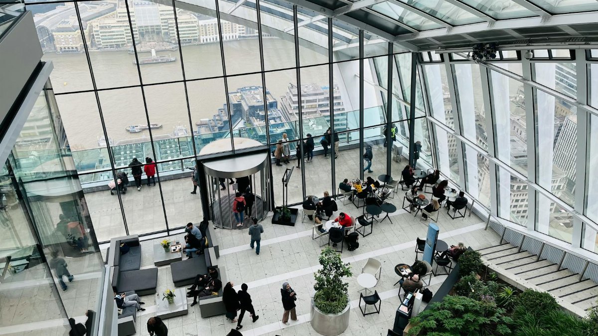 A bustling indoor observation deck overlooking the Thames River in London with city views.