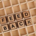 Wooden letter blocks spelling 'Feedback' on a wooden grid surface.