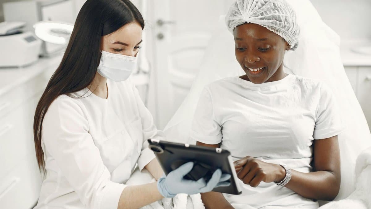 Smiling patient and dermatologist using tablet during skincare consultation.