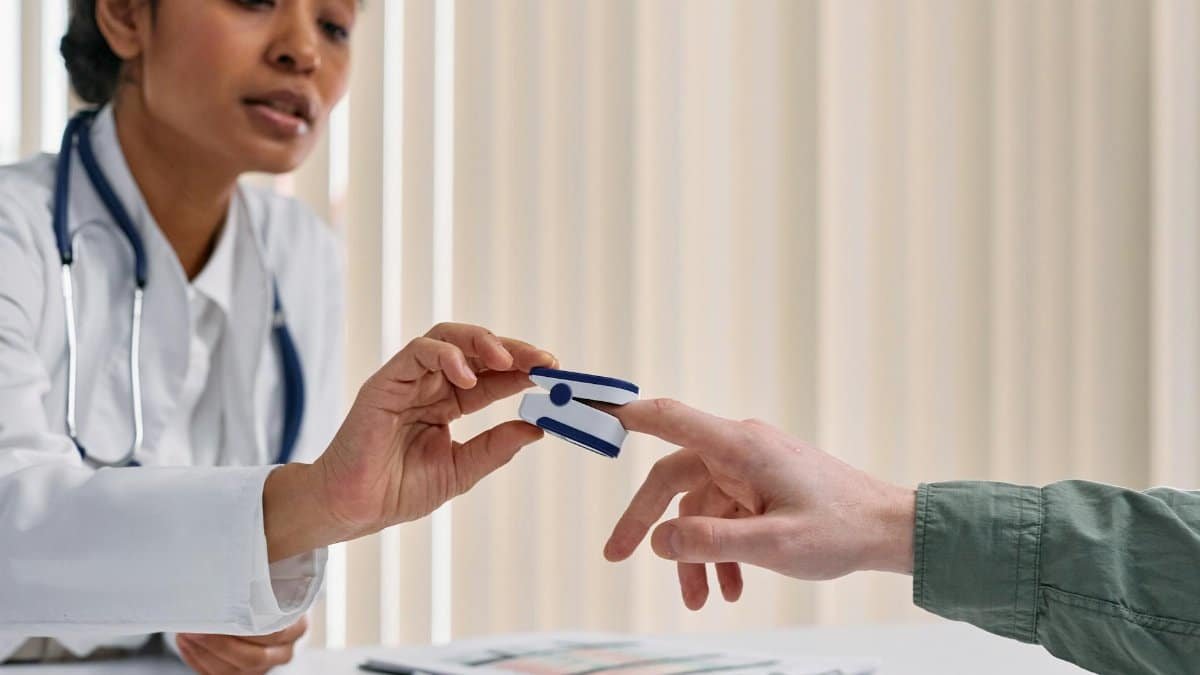 Healthcare worker checking patient vitals with a pulse oximeter in a clinical setting.