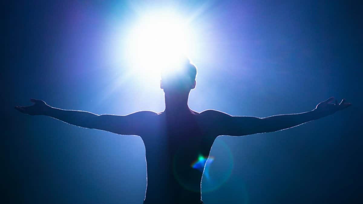 Silhouette of a man with arms raised, backlit by bright sun, creating an artistic effect.