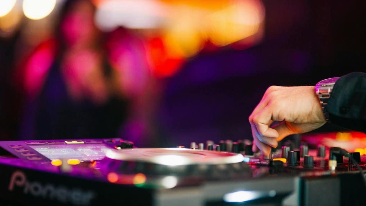 Hand of DJ mixing music on turntable at a lively nightclub event