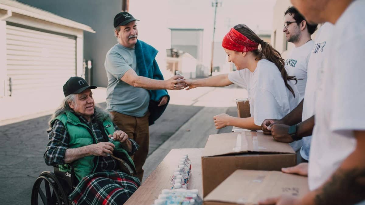 Volunteers distribute water and supplies to people outdoors, promoting community support and kindness.