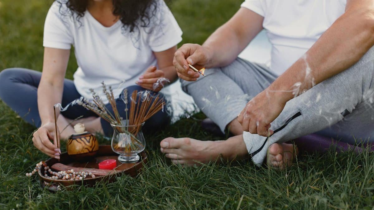 A couple practicing meditation with incense sticks and prayer beads outdoors, creating a peaceful atmosphere.