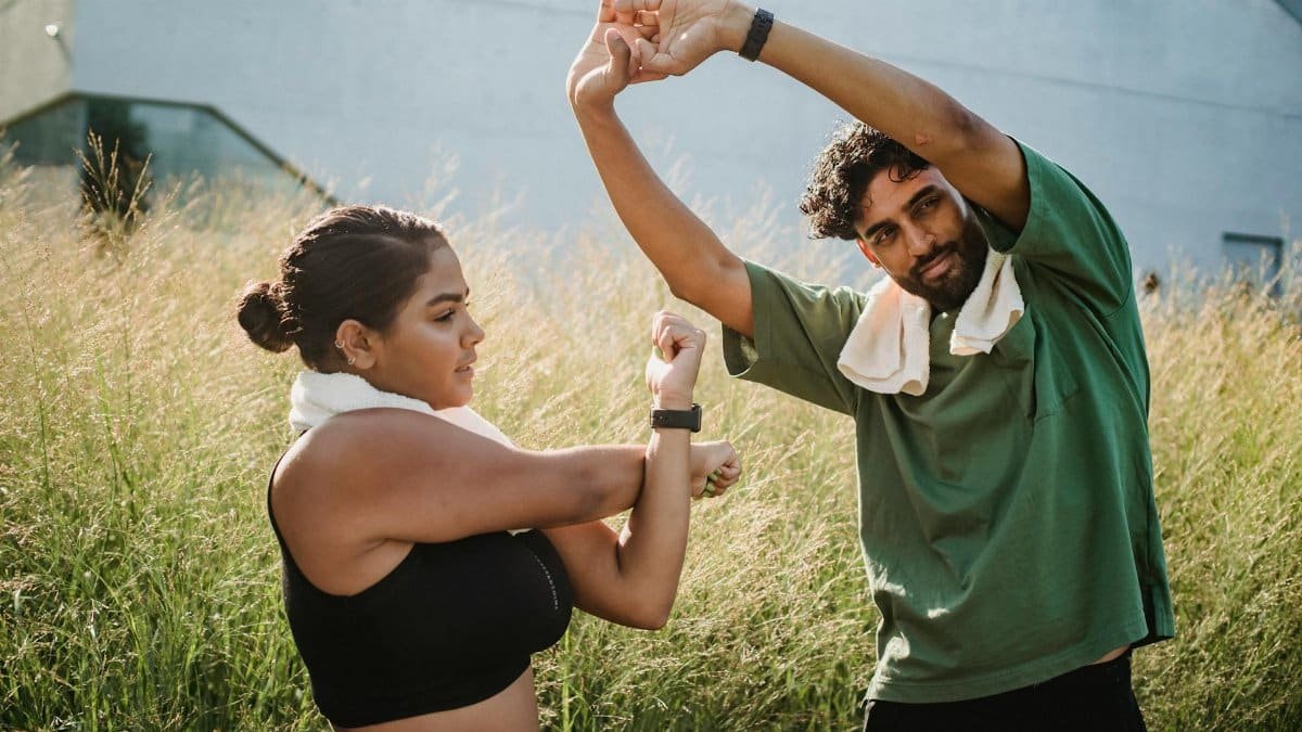 A couple engaging in outdoor stretching exercises surrounded by tall grasses on a sunny day.