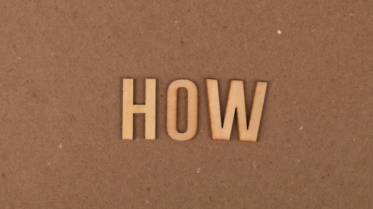 Wooden letters spelling 'HOW' on brown textured cardboard background.