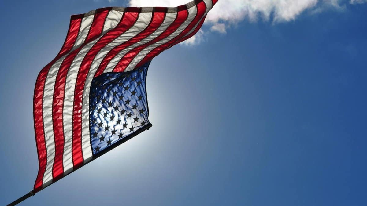 Low-angle view of the American flag waving against a bright blue sky on a sunny day.