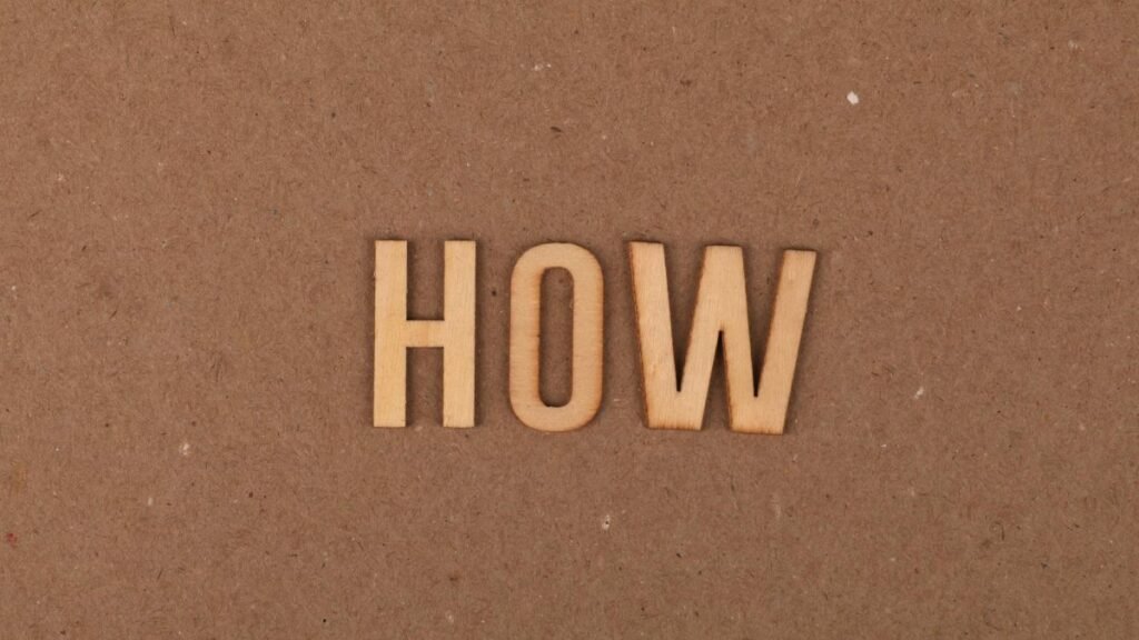 Wooden letters spelling 'HOW' on brown textured cardboard background.
