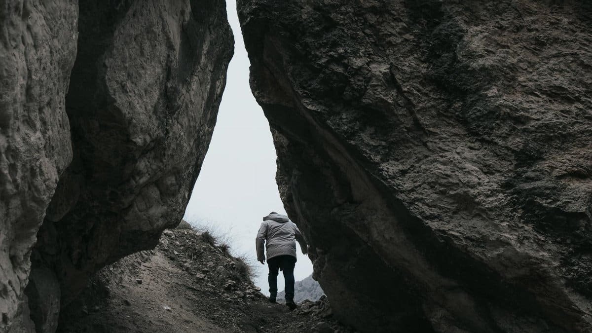 A lone man climbs through a narrow rocky passage in the mountains, symbolizing adventure.
