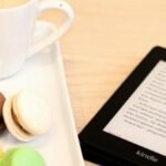 Cozy setup with coffee, colorful macarons, and Kindle e-reader on table.