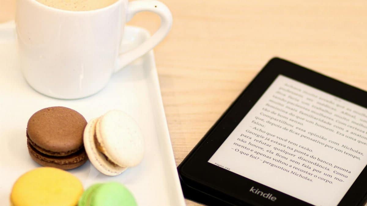 Cozy setup with coffee, colorful macarons, and Kindle e-reader on table.