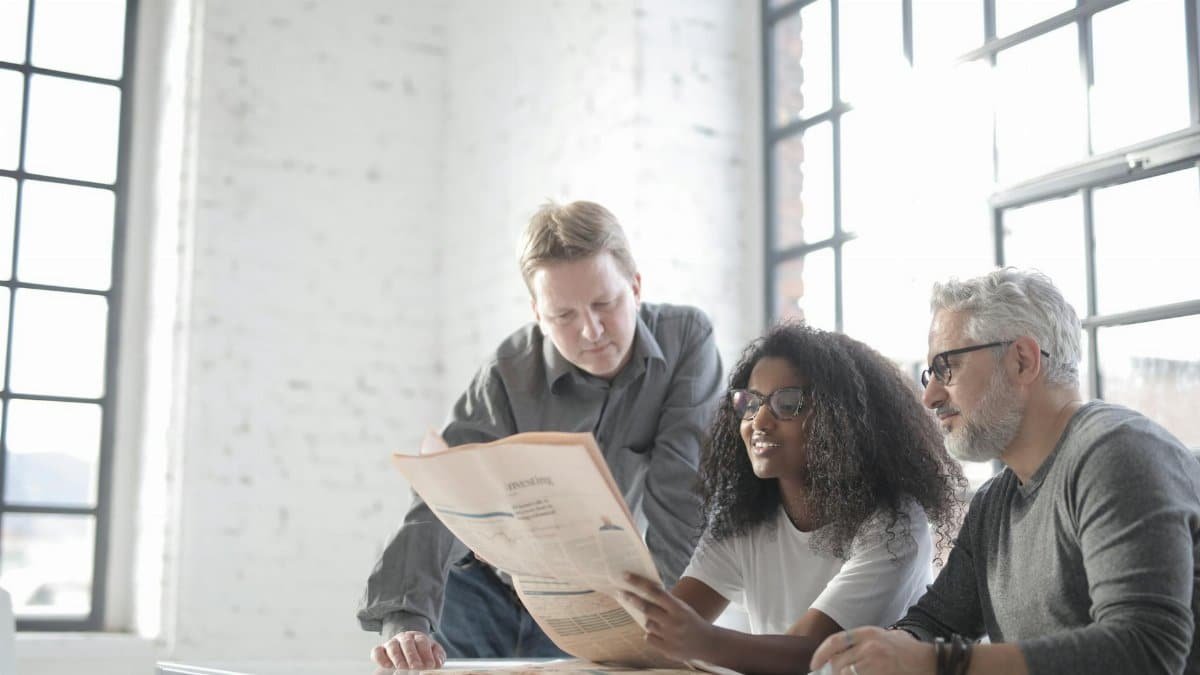Group of journalists of different ages in informal clothes doing paperwork while spending time together in modern workspace together in daytime
