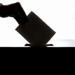Silhouette of a hand placing a vote into a ballot box, symbolizing democracy.