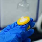 Detailed close-up of a hand in a blue glove holding a laboratory syringe filter indoors.