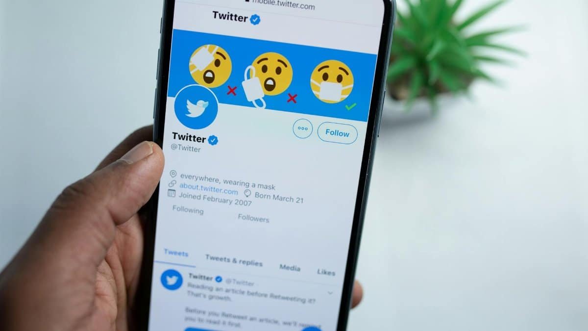 A close-up of a hand holding a smartphone showing a Twitter profile, emphasizing social media engagement.