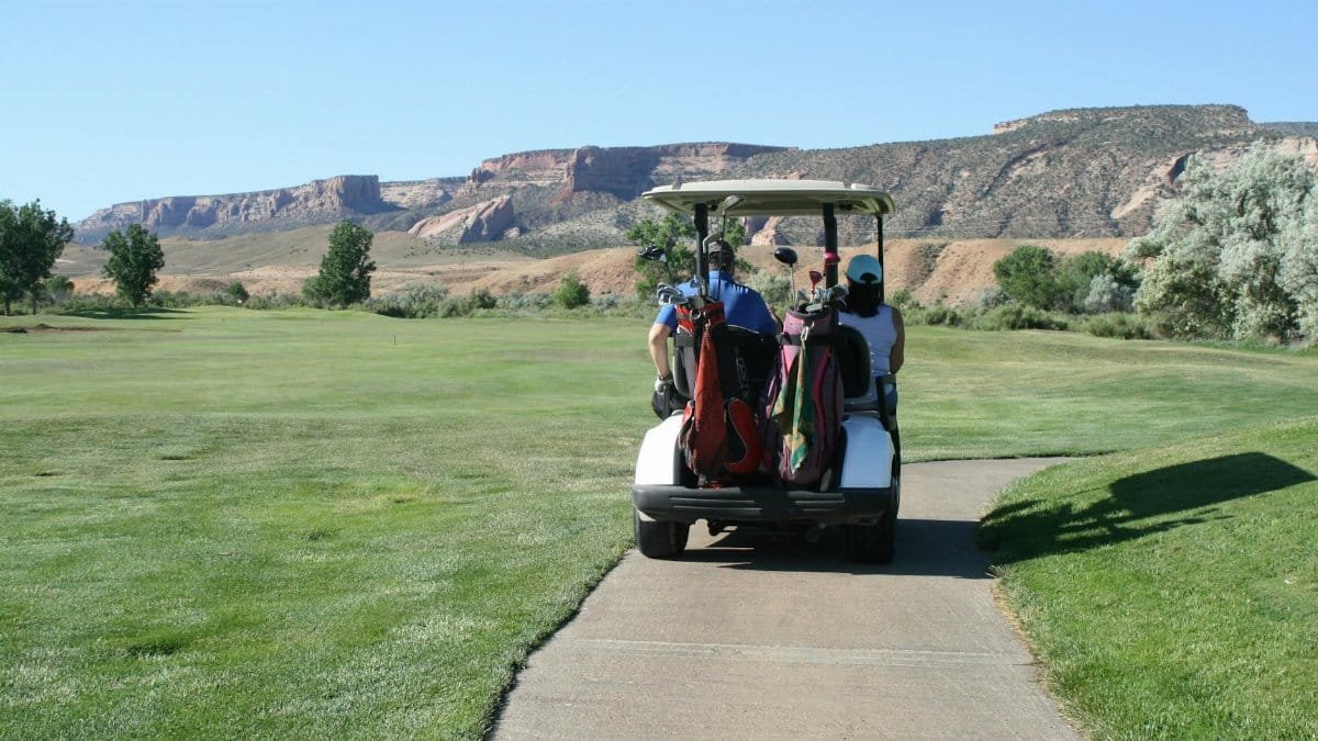 Golfers riding on a cart across a scenic golf course with mountain backdrop.