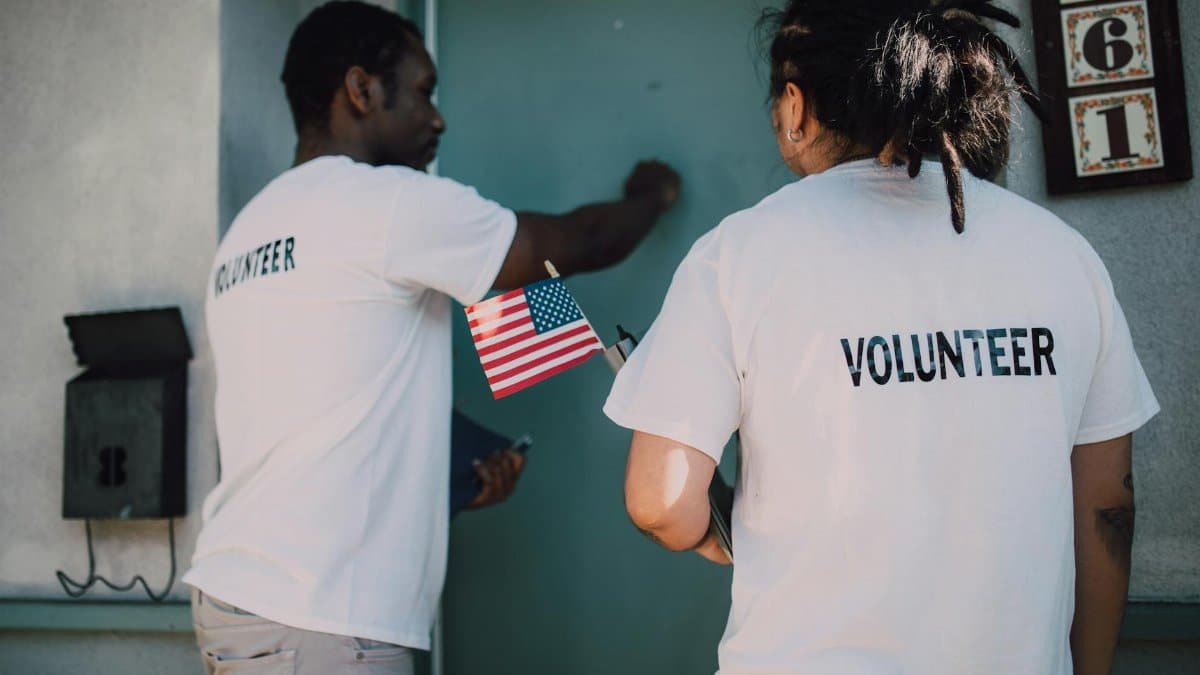 Two volunteers knocking on door during a community outreach event, holding a small American flag.